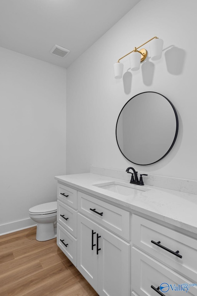 bathroom featuring visible vents, wood finished floors, vanity, baseboards, and toilet