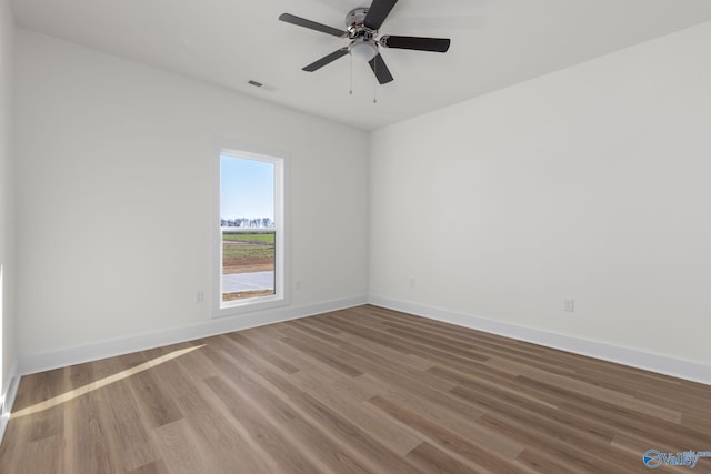 spare room with baseboards, a ceiling fan, wood finished floors, and visible vents