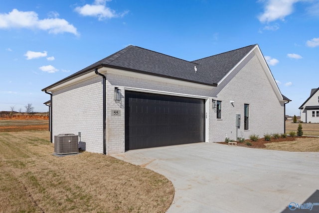 view of side of home featuring brick siding, a garage, central AC unit, concrete driveway, and a yard