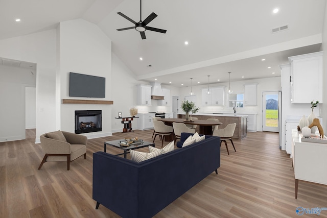 living area featuring a fireplace, ceiling fan, high vaulted ceiling, recessed lighting, and light wood finished floors
