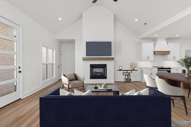 living room featuring ceiling fan, a fireplace, high vaulted ceiling, baseboards, and light wood-type flooring