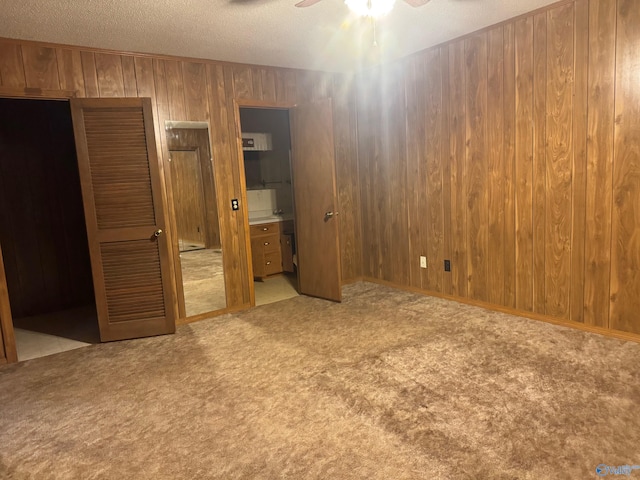 unfurnished bedroom featuring light carpet, connected bathroom, ceiling fan, and wood walls