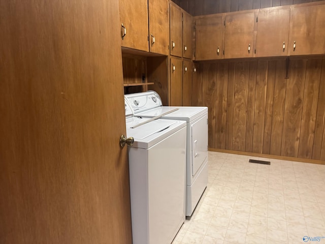 washroom with washer and dryer, cabinets, and wooden walls