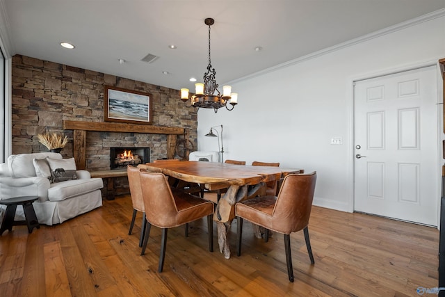 dining area with visible vents, baseboards, ornamental molding, a stone fireplace, and wood finished floors