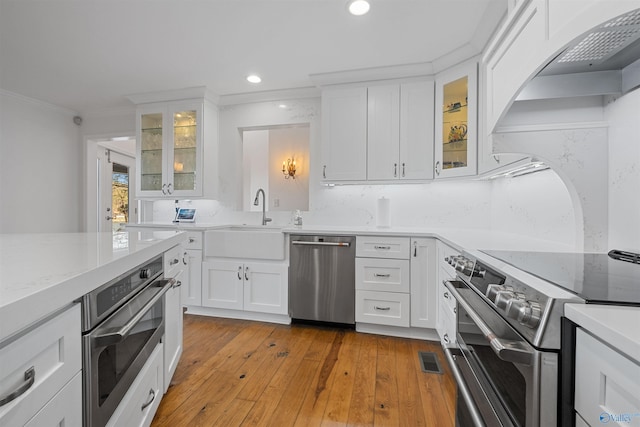 kitchen with white cabinets, stainless steel appliances, light wood-style floors, and a sink