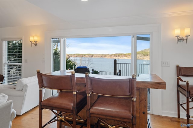 dining area with baseboards, light wood-style floors, a water view, and ornamental molding