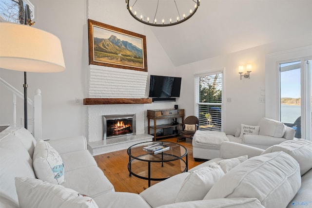 living room featuring a glass covered fireplace, an inviting chandelier, wood finished floors, and high vaulted ceiling