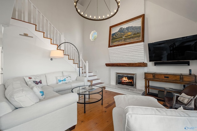 living room featuring a notable chandelier, a glass covered fireplace, hardwood / wood-style floors, stairway, and a towering ceiling