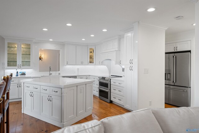 kitchen featuring light countertops, appliances with stainless steel finishes, wood finished floors, white cabinets, and a sink