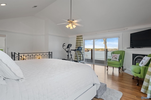 bedroom with access to exterior, visible vents, lofted ceiling, a fireplace, and wood finished floors