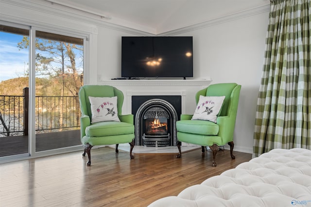 living area with crown molding, wood finished floors, and a lit fireplace