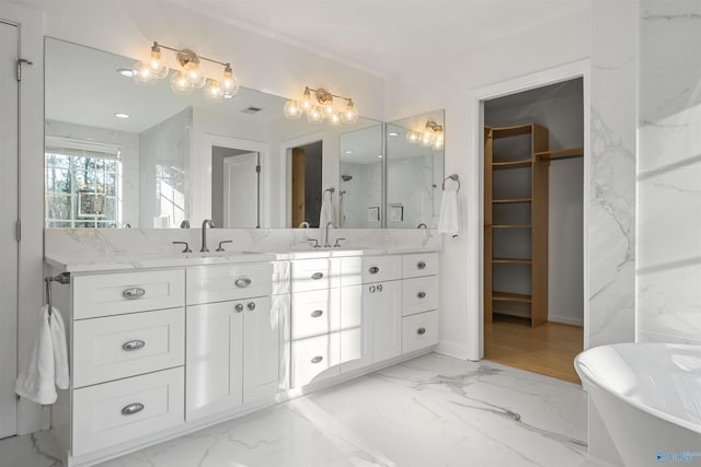 full bath with marble finish floor, a sink, double vanity, a freestanding bath, and a spacious closet