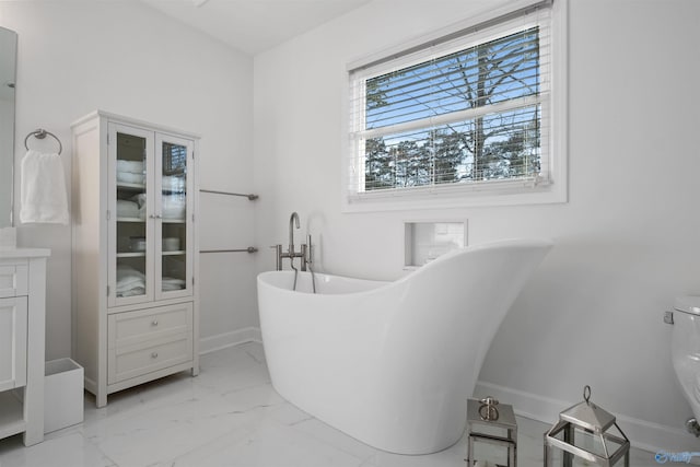 bathroom featuring baseboards, toilet, a freestanding tub, marble finish floor, and vanity