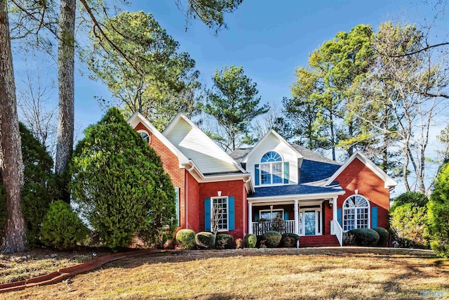 traditional-style home featuring covered porch, brick siding, and a front yard