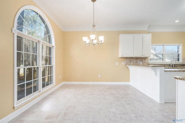 unfurnished dining area with a notable chandelier, crown molding, baseboards, and a sink