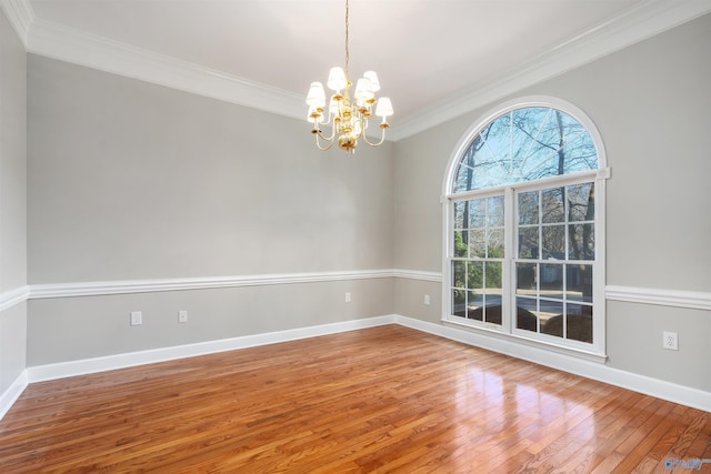 spare room featuring wood-type flooring, crown molding, baseboards, and an inviting chandelier