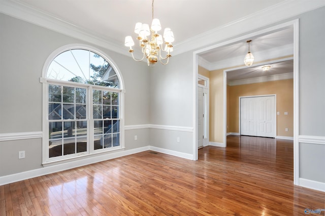 spare room with crown molding, baseboards, a notable chandelier, and hardwood / wood-style floors