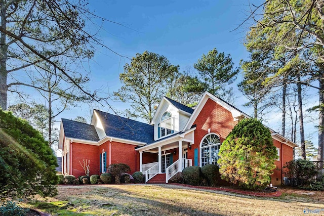 view of front of home with covered porch, brick siding, and a front lawn