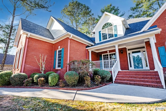 view of front of house featuring roof with shingles, a porch, and brick siding