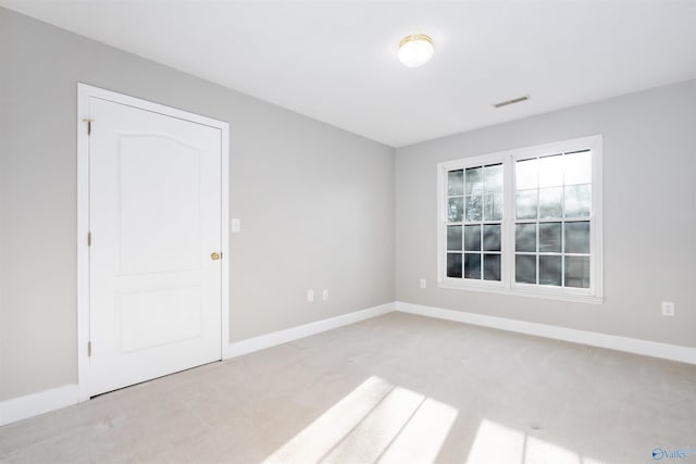 spare room featuring baseboards, visible vents, and light colored carpet