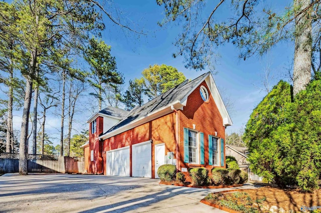 view of side of home featuring driveway, a garage, fence, and brick siding