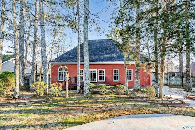 view of front facade featuring brick siding, a shingled roof, and fence