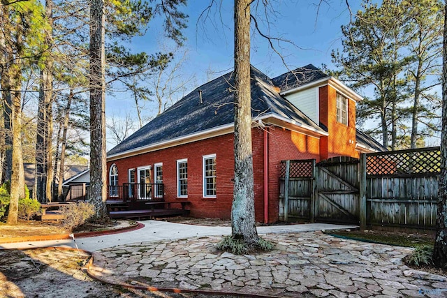 view of property exterior featuring a gate, brick siding, fence, and a deck