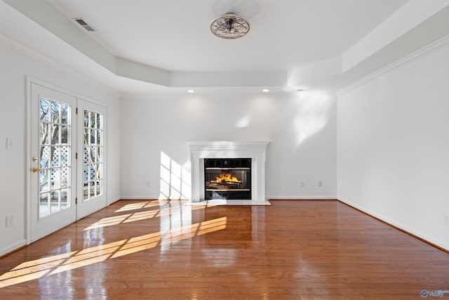 unfurnished living room featuring wood-type flooring, ornamental molding, and a raised ceiling