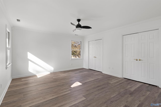 unfurnished bedroom with multiple closets, crown molding, ceiling fan, and dark hardwood / wood-style flooring