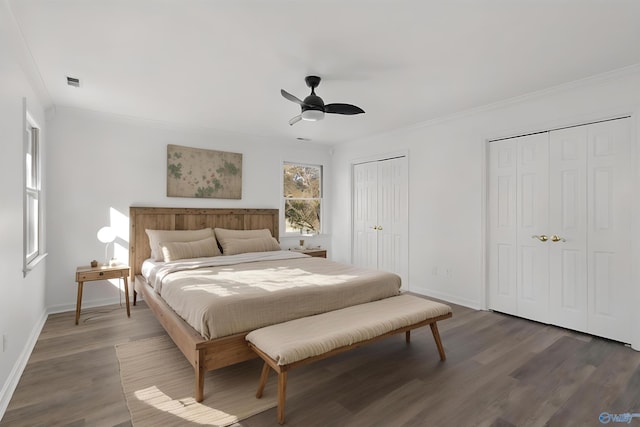 bedroom with ceiling fan, ornamental molding, dark hardwood / wood-style floors, and two closets