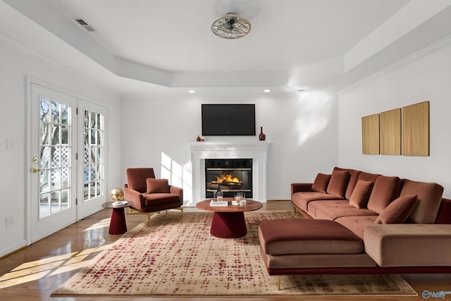 living room featuring a tray ceiling, crown molding, wood-type flooring, and french doors