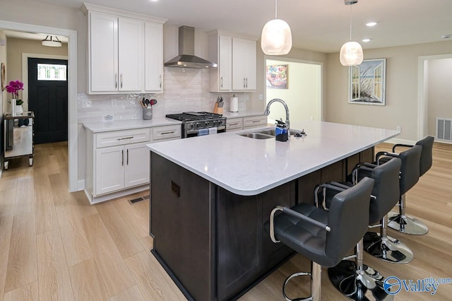 kitchen with high end range, white cabinets, sink, wall chimney exhaust hood, and decorative light fixtures