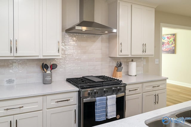 kitchen with stainless steel range, backsplash, white cabinets, and wall chimney range hood