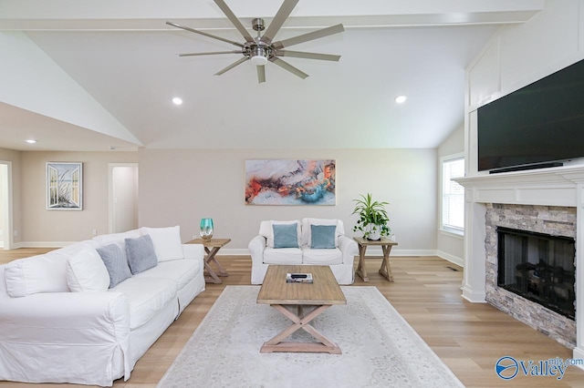 living room with ceiling fan, beam ceiling, high vaulted ceiling, light hardwood / wood-style flooring, and a stone fireplace