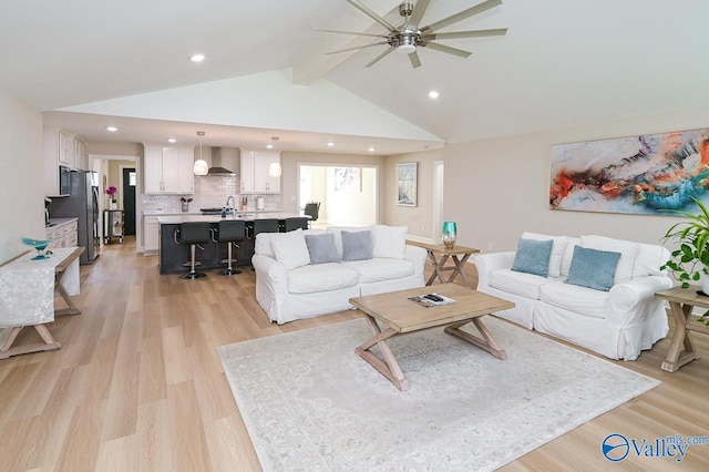 living room featuring lofted ceiling with beams, light hardwood / wood-style floors, sink, and ceiling fan