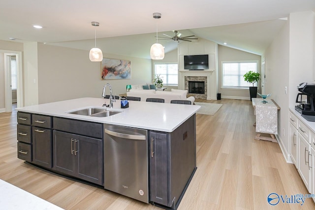 kitchen featuring pendant lighting, dishwasher, sink, vaulted ceiling, and a fireplace