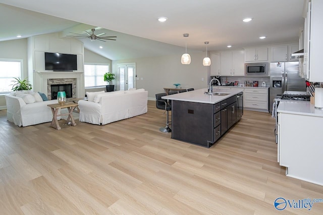 kitchen featuring sink, vaulted ceiling, a kitchen island with sink, white cabinets, and appliances with stainless steel finishes