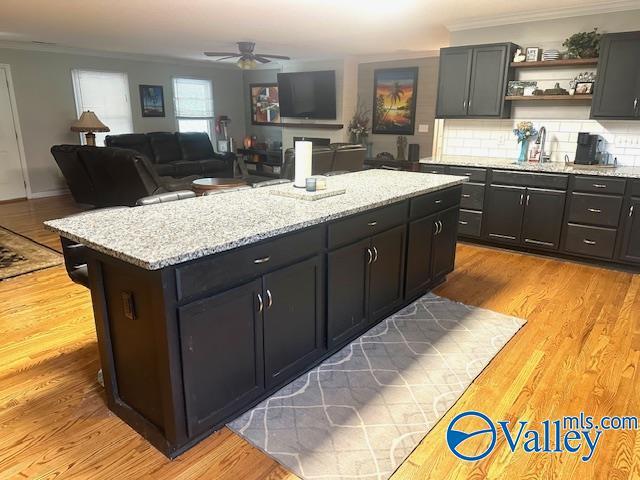 kitchen with ceiling fan, a center island, tasteful backsplash, crown molding, and light wood-type flooring