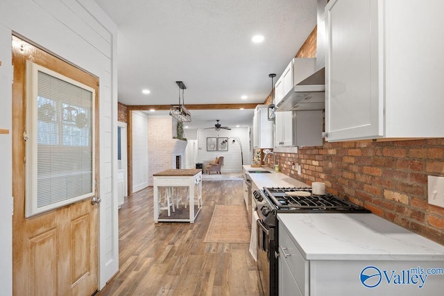 kitchen featuring white cabinetry, stainless steel gas range, hanging light fixtures, light stone countertops, and sink