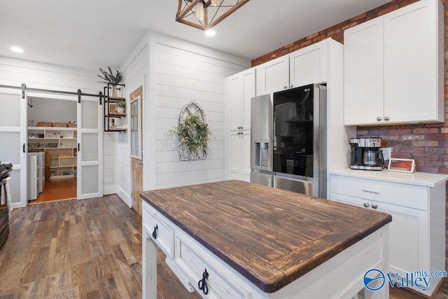 kitchen with a barn door, wooden counters, dark hardwood / wood-style floors, white cabinetry, and stainless steel fridge