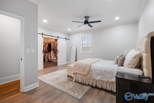 bedroom featuring ceiling fan, a barn door, wood-type flooring, a walk in closet, and a closet