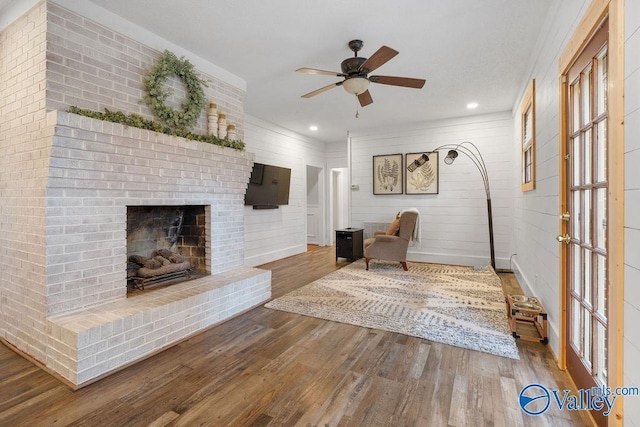 unfurnished living room with hardwood / wood-style flooring, a brick fireplace, ceiling fan, and wooden walls