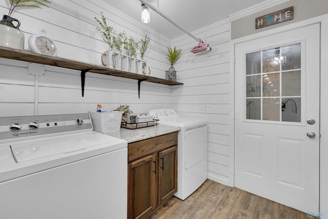 laundry area featuring cabinets, wooden walls, separate washer and dryer, and light hardwood / wood-style floors