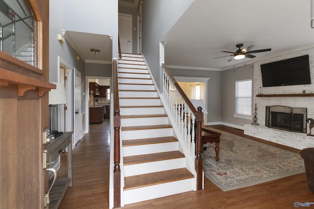 staircase featuring ceiling fan, crown molding, wood-type flooring, and a brick fireplace