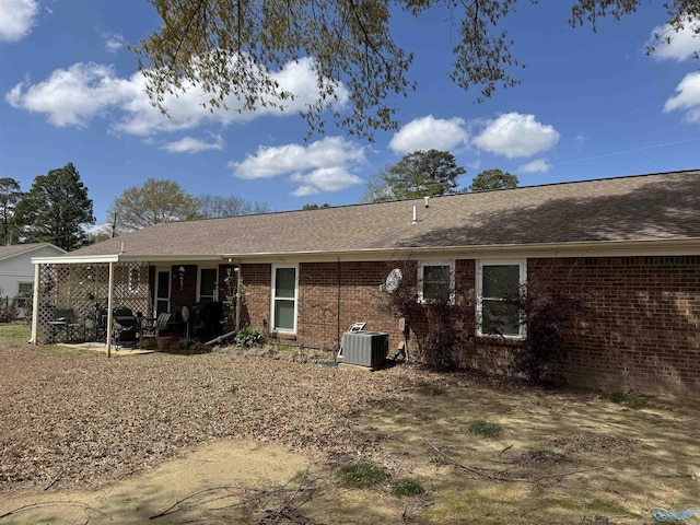 rear view of property with central air condition unit, roof with shingles, and brick siding