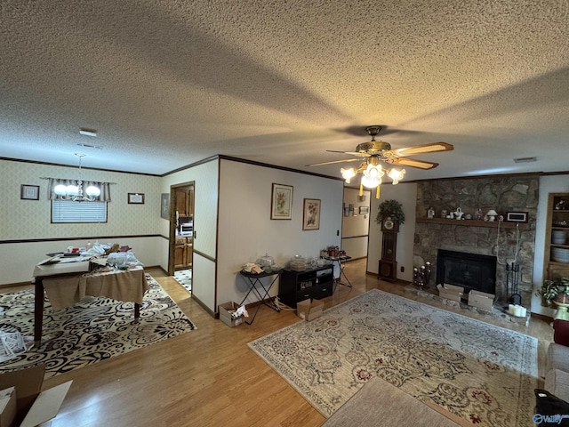 living room with crown molding, a stone fireplace, wood finished floors, and wallpapered walls