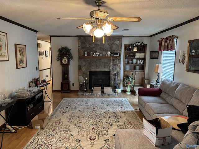 living room with a stone fireplace, ornamental molding, a textured ceiling, a ceiling fan, and wood finished floors
