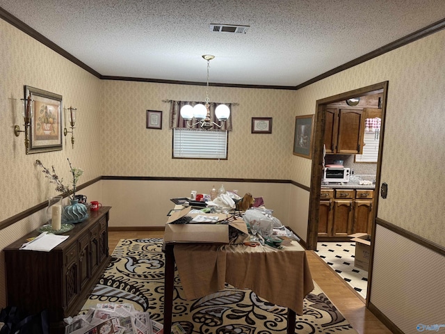 dining area with wallpapered walls, a chandelier, a textured ceiling, visible vents, and wainscoting
