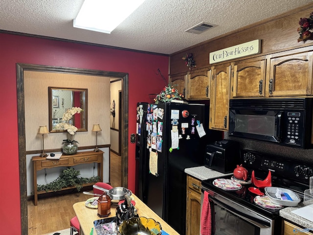 kitchen with visible vents, light countertops, a textured ceiling, black appliances, and wood finished floors
