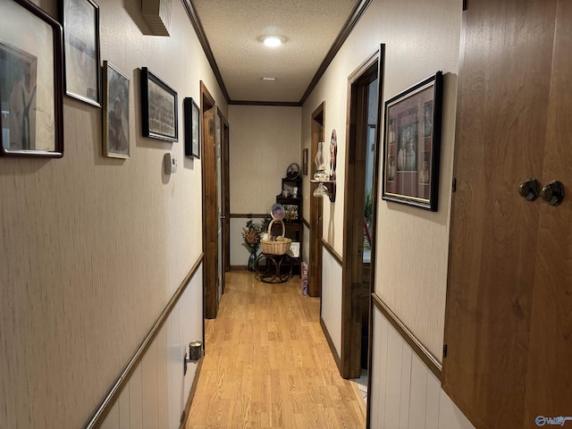 hall with light wood-style floors, a textured ceiling, crown molding, and a wainscoted wall